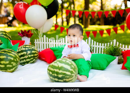 Glückliches Kind mit großen roten Scheibe Wassermelone sitzen auf grünem Gras im Sommer Park. Gesunde Ernährung Konzept. Stockfoto
