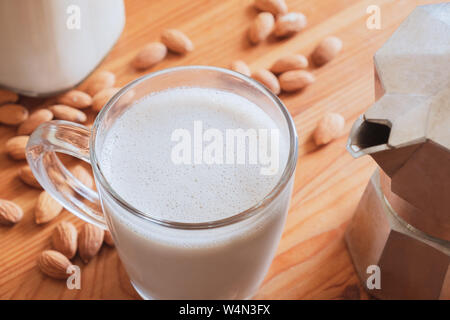 Glas Mandelmilch und Kaffeemaschine auf Holz Tisch. Vegan Mandel trinken und Espresso Moka Teekocher - auf Basis pflanzlicher Ersatz für Kaffee Stockfoto