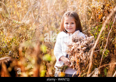 Foto von glücklichen kleinen Mädchen unter Herbst gelb trockenen Pflanzen posing Stockfoto