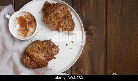 Hintergrund der nahrhaften Frühstück mit Croissants und eine warme Tasse Cappucino bestreut mit Zimt auf Holz- Oberfläche. Stockfoto