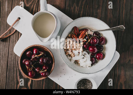 Gesund Sommer vegetarisches Frühstück mit Müsli, Kirsche, Pekannüsse, Kokosraspeln, Chia und hafermilch auf Marmor Fach. Stockfoto