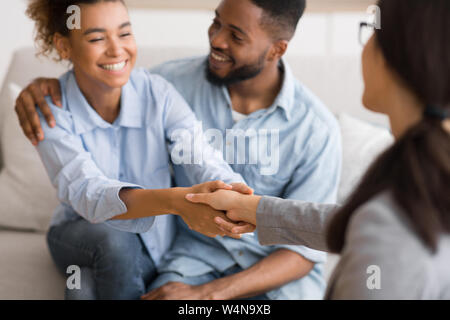 Dankbarkeit für professionelle Hilfe. Happy afro Paar und Psychologe handshaking im Amt nach der effektiven Therapie. Selektiver Fokus Stockfoto