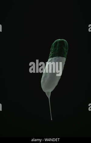 Grüne Gurke Tropfen weißer Farbe auf einem schwarzen blackground. Stockfoto