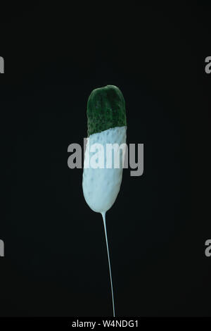 Grüne Gurke Tropfen weißer Farbe auf einem schwarzen blackground. Stockfoto