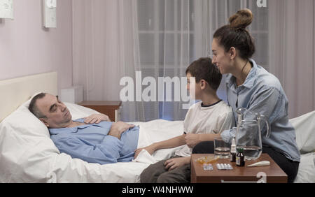 Ältere Menschen liegen auf dem bequemen Bett im eigenen Krankenhaus, umarmen kleine Enkel Stockfoto