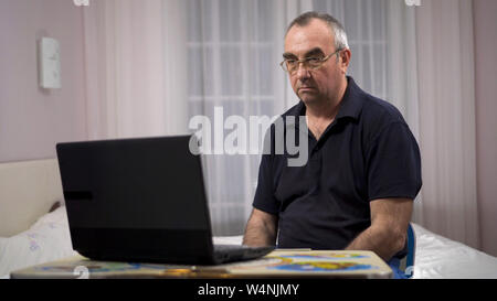 Ältere grauhaarige Mann mit Laptop,, Fußball auf einem Laptop und erhält umgekippt Stockfoto