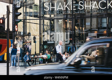 London, UK - 15. Juli 2019: Black Cab vorbeifahren Shake Shack in der Victoria Station, Bewegungsunschärfe. Shake Shack ist eine US-amerikanische Fast-Food-Restaurant kette Stockfoto