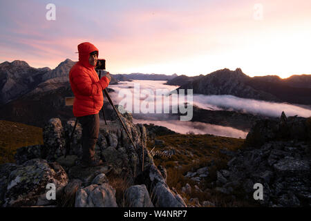 Mann Fotografieren Nebeln bei Sonnenaufgang vom Gipfel der Berge Stockfoto