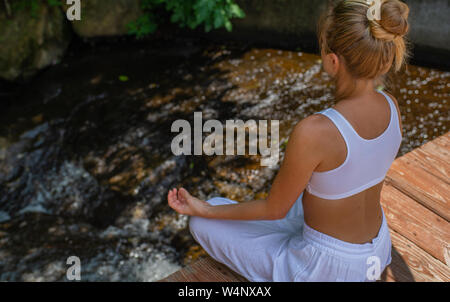 Attraktive Frau ist Yoga und Meditation im Lotussitz sitzen in der Nähe des Wasserfalls. Junge Frau ist Meditation im Freien am Morgen. Stockfoto