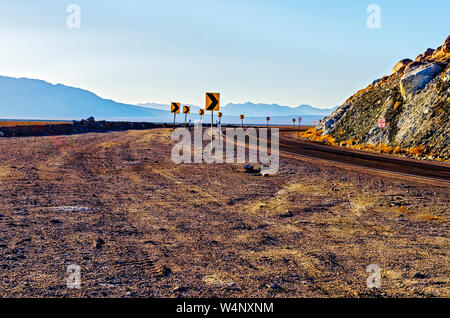 Desert highway geschwungene Um felsige Hügel mit hazy Wüste Berge. Pfeil Zeichen, geschwungene Straße. Stockfoto