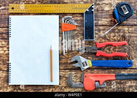 Alte Werkzeuge, Zangen, Maßband, verstellbarer Schraubenschlüssel, eine Reihe von Hex-Tasten auf ein leeres Notebook mit einem Bleistift vor dem Hintergrund eines alten Stockfoto