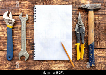 Alte Handwerkzeuge, Hammer, Blechschere, Rollgabelschlüssel, Johannisbrot Schraubenschlüssel Surround ein leeres Notebook mit einem Bleistift vor dem Hintergrund einer alten hölzernen Stockfoto