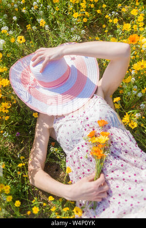 Blick von oben auf eine schöne Frau in Kleid lag in der Wiese mit Blumen an einem sonnigen Tag Stockfoto