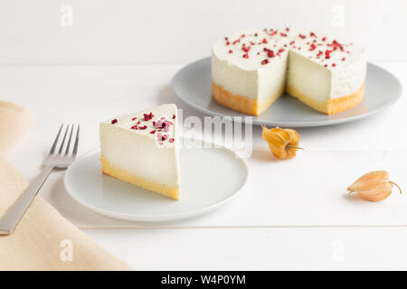 Stück Käsekuchen mit Matcha mit getrockneten Beeren auf der Oberseite und weiß Becher Kaffee auf weißem Hintergrund Stockfoto