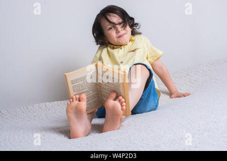 Kleiner Junge mit Buch auf Füße wie Bildung Konzept Stockfoto