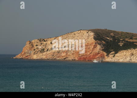 Kleines Boot neben dem roten Felsen auf Milos Stockfoto