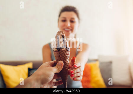 Mann gibt Schokolade Eis in Kegel zu seiner Freundin zu Hause. Sharing Dessert. Close Up. Stockfoto