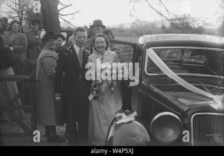 1950, historische, nur ein paar außerhalb von ihren Austin Auto verheiratet, mit Bändern verziert, mit Hochzeit Gäste auf, England, UK. Stockfoto