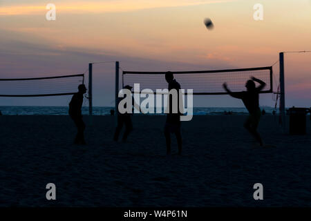 Silhouetten der vier Volleyballer spielen am Strand bei Sonnenuntergang mit Blick auf den Ozean und einen bunten Himmel im Hintergrund. Huntington Beach, CA. Stockfoto