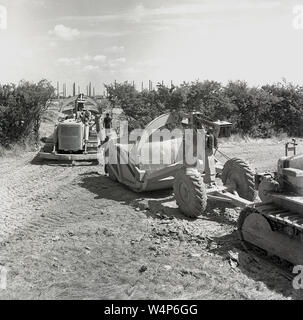 1950, historische, Arbeitnehmer und Baumaschinen draußen in der Landschaft an der London Brick Company, Bedford, England, UK, mit der industriellen Komplex Schornsteine in der Ferne. Stockfoto