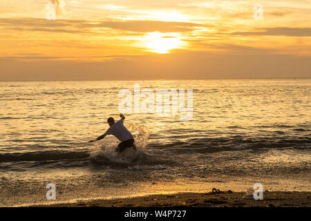 Aberystwyth, Wales, UK. 24. Juli 2019. Junge Männer überfliegen - Boarding auf die Wellen, wie sie auf dem Strand in Aberystwyth bei Sonnenuntergang brechen auf einer weiteren heißen Tag wie eine Wolke aus heißer Luft weiterhin vom Kontinent zu driften. Temperaturen werden erwartet, die hohe 30 Celsius in Teilen zu erreichen, wenn die süd-östlich von Großbritannien am Donnerstag, 25. Juli. Foto Keith Morris/Alamy leben Nachrichten Stockfoto