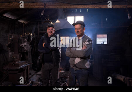 Porträt von zwei Generationen zuversichtlich Schmied stand mit verschränkten Armen in der traditionellen Workshop Stockfoto