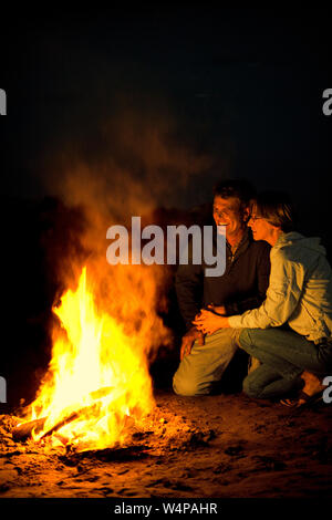 Lächelnd Mann und Frau in der Nähe von einem Lagerfeuer am Strand sitzen. Stockfoto