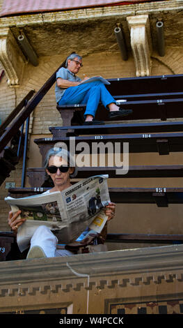 Mann und Frau lesen Zeitungen in den Zuschauertribünen auf der Piazza de Campo während des Wartens auf den Beginn der Palio in Siena, Italien Stockfoto