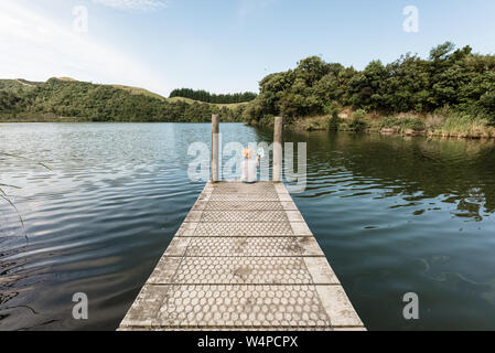 Kleinkind Junge sitzt auf einem hölzernen Dock an einem See Stockfoto