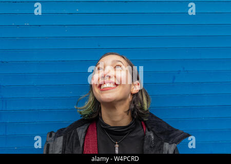 Lächelnde Frau sucht auf der Regen auf ihrem Gesicht, auf der blauen Wand. Stockfoto
