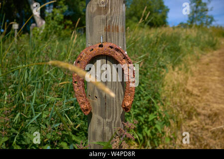 Altes rostiges Hufeisen genagelt hölzerne Stange auf einem Gras Hügel in der Nähe der Straße Stockfoto