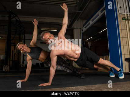 Einen mittleren Alters attraktiv und sportlich Paar ist Partner Training zusammen tun in ein Fitnessstudio. starker Mann und Frau sind Lachen und dabei t-Push-ups. Stockfoto