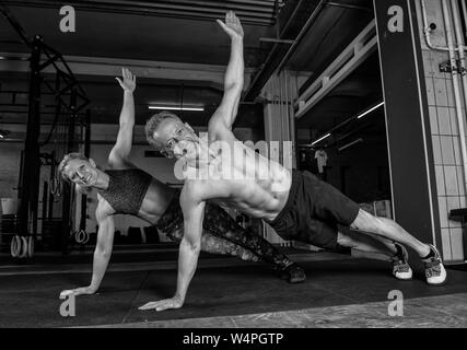 Einen mittleren Alters attraktiv und sportlich Paar ist Partner Training zusammen tun in ein Fitnessstudio. starker Mann und Frau sind Lachen und dabei t-liegestütze. Stockfoto