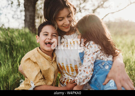 Mutter, Sohn und Tochter kuscheln auf der Decke im Feld mit Hintergrundbeleuchtung Stockfoto