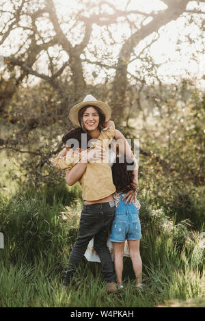 Die volle Länge der Mutter umarmt Sohn und Tochter im Feld mit Hintergrundbeleuchtung Stockfoto