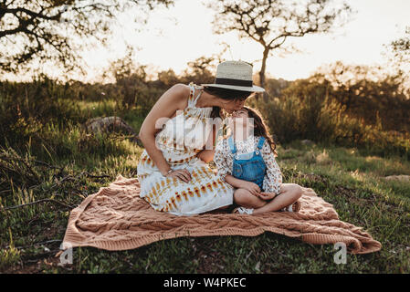 Mutter und Tochter sitzen auf Decke in Feld küssen Stockfoto