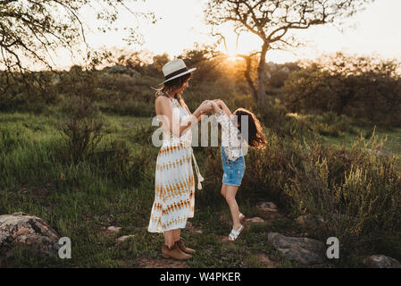 In voller Länge ansehen der jungen Mutter und Tochter springen in sonnige Wiese Stockfoto
