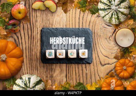Rahmen der Blätter und Kürbisse, ein schiefer Platte mit der Meldung 'Herbst' in Deutsch und Würfel mit Kochen Symbole auf Holz- Hintergrund Stockfoto