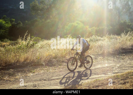 Reifer Mann reiten Mountainbike gegen helles Sonnenlicht auf Trail in CA Stockfoto