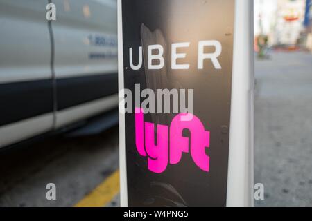 Nahaufnahme der Vertikalen mit Logos für ridesharing Unternehmen Uber und Lyft, mit Rädern eines Autos im Hintergrund, dass ein Ort, wo rideshare Pickups in der Innenstadt von Los Angeles, Kalifornien, 24. Oktober 2018 zur Verfügung stehen. () Stockfoto
