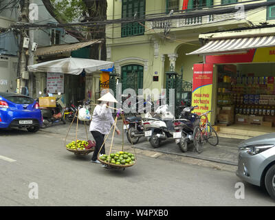 HANOI, VIETNAM - 28. JUNI 2017: eine Frau, die mit einem Schulter- und zwei Körbe entlang einer Straße in Hanoi Obst Stockfoto