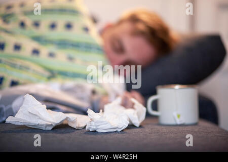 Ein junger Mann, krank im Bett, unscharf, Gewebe und Tee Tasse im Fokus ist. Stockfoto