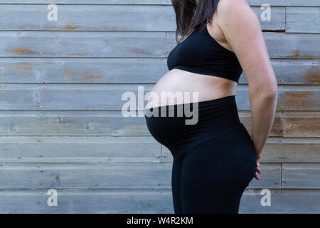 Schwangere Frau spät im dritten Trimester mit schwarzen stretch Mutterschaft Hosen. Stockfoto