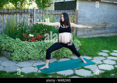 Schwangere Frau spät im dritten Trimester Üben der Krieger II darstellen, virabhadrasana II, in einer friedlichen Atmosphäre an einem Sommerabend. Stockfoto