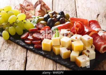 Antipasti snack Teller mit Käse, Schinken, Trauben, Feigen, Oliven, Würste und close-up auf einem Holztisch. Horizontale Stockfoto