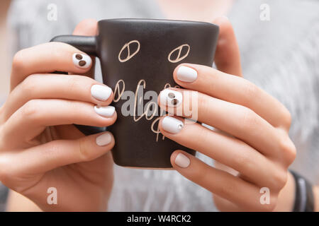 Weibliche Hände mit weißen Nail Design holding Schwarze Schale Stockfoto