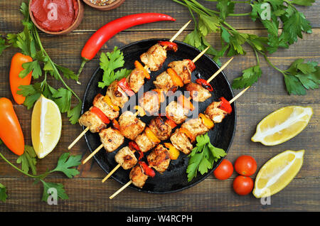 Gegrilltes Hühnchen Kebab mit Paprika in der Pfanne, Gemüse und Kräutern auf Holztisch, Ansicht von oben Stockfoto