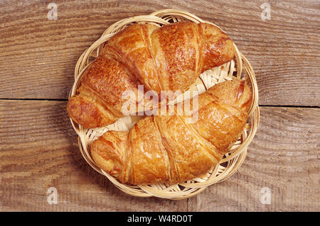 Zwei frische Croissants in wicker Platte auf Holz- Hintergrund, Ansicht von oben Stockfoto