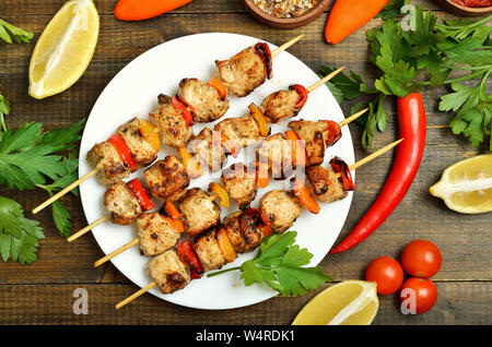 Gegrilltes Hühnchen Kebab mit Paprika auf weiße Platte, Gemüse und Kräutern auf Holztisch, Ansicht von oben Stockfoto