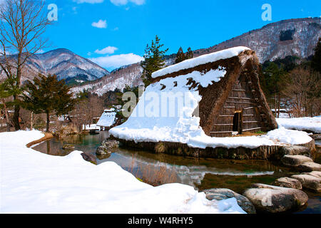 Holz- dorf Unterstand mit Strohdach umgeben von Wasser mit Blick auf die Berge am Horizont im Winter, Shirakawa Dorf, Ono Bezirk Stockfoto